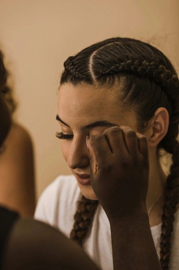 A woman with braids putting makeup on her face.